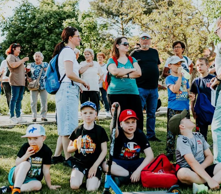A diverse group of families and children enjoying an outdoor event on a sunny day in a park setting.