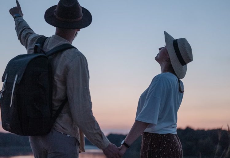 Romantic couple holding hands while watching a sunset at a serene lakeside location, embracing nature.