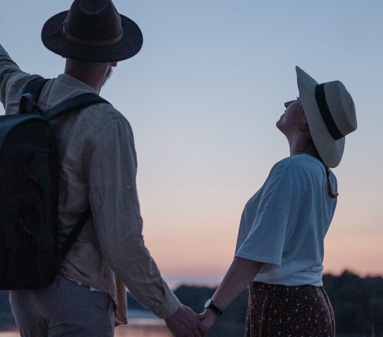 Romantic couple holding hands while watching a sunset at a serene lakeside location, embracing nature.